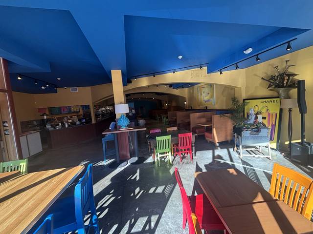 The dining room, with colorful chairs, booths, and the counter under a blue ceiling