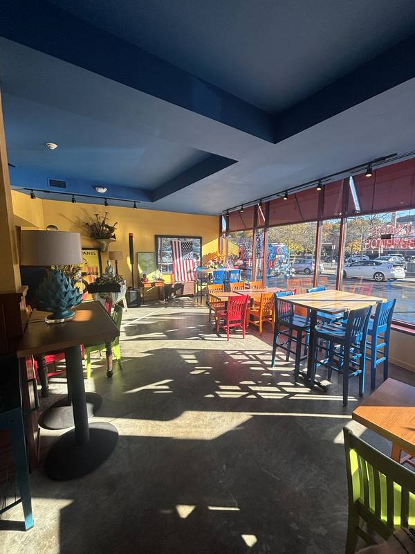 Sunlit window tables on Langley Road with red, orange, and blue chairs